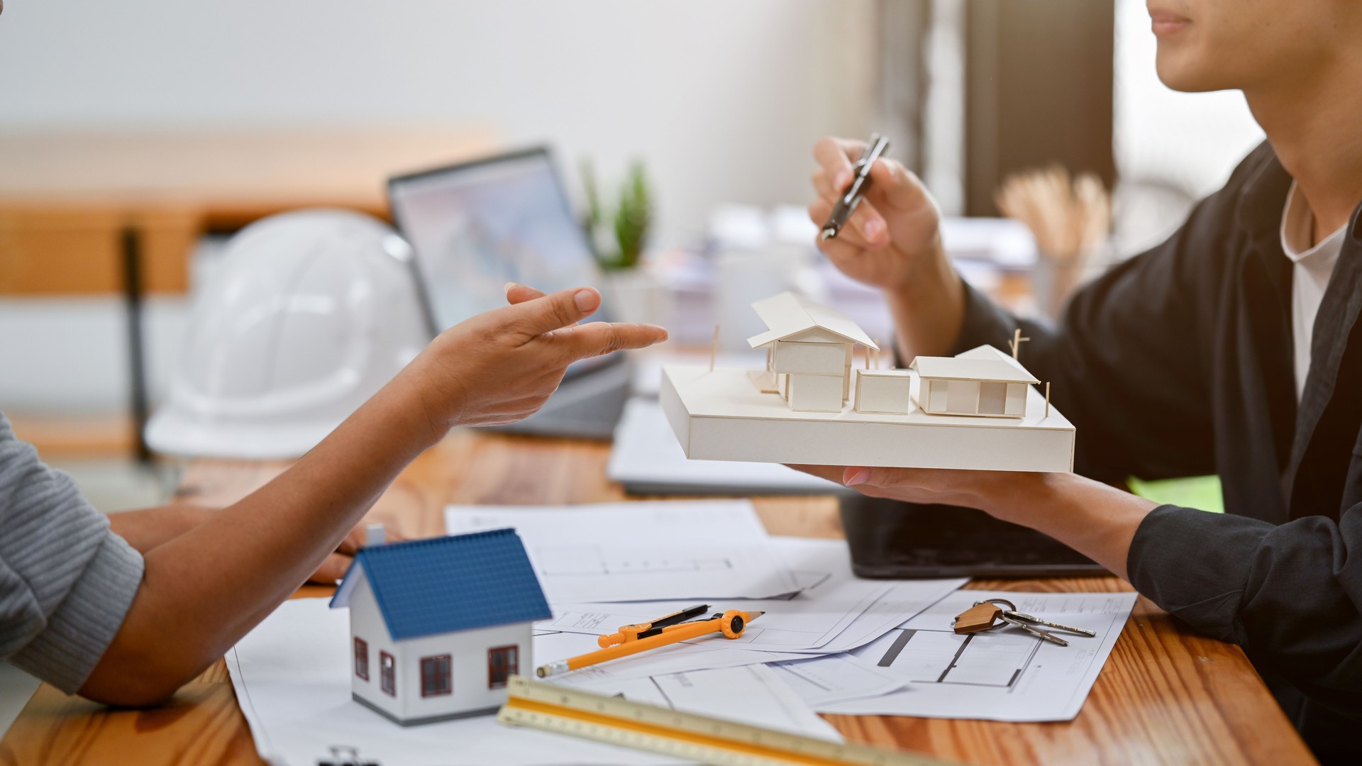 A male architect is showing a house model to a client while discussing the building designs.